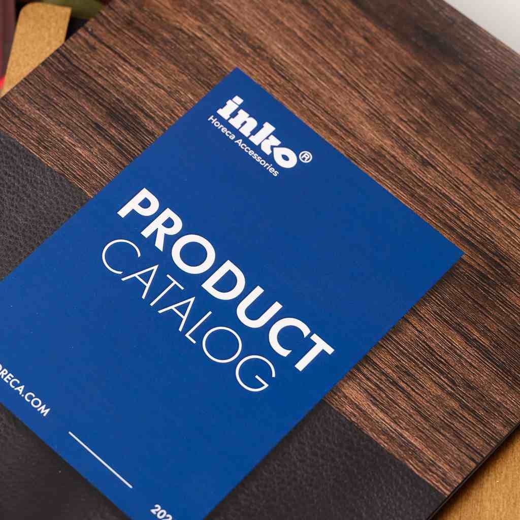 A close-up shot of the "Inko Horeca Accessories" Product Catalog cover. The design features a premium blue card overlay with white typography on a background of dark textured wood and black leather-like material.