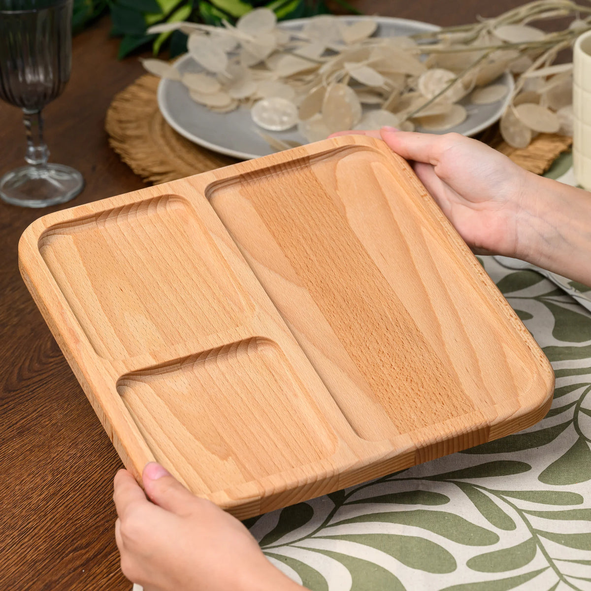Hands lifting an empty beech wood serving board at an angle, showing all three compartments and rounded edges