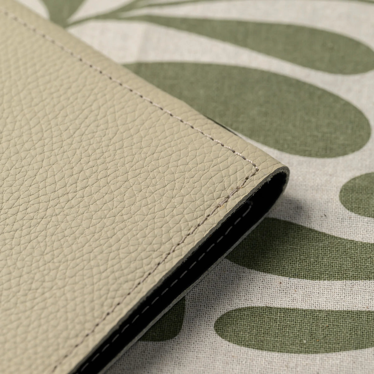 Beige leather cover edge folding over black inner lining, stitched border visible on a green leaf-print tablecloth