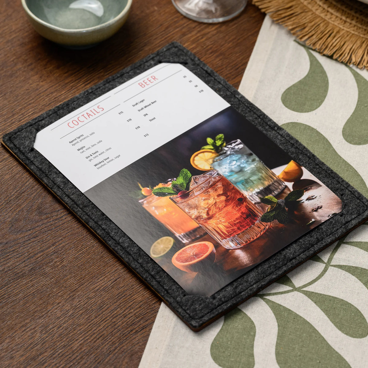 An overhead view of a felt menu board with a printed page, resting beside a ceramic bowl and glass