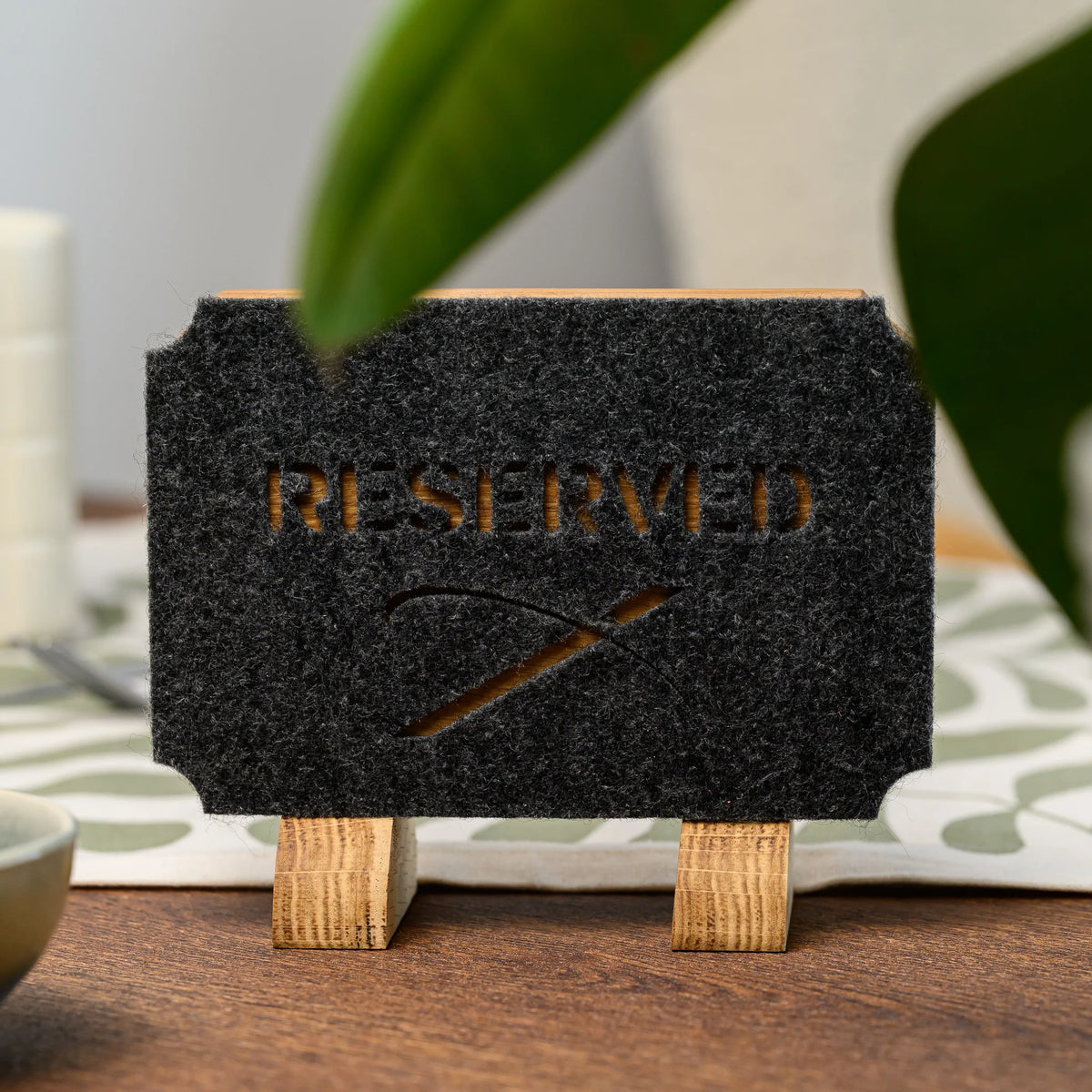 A Reserved table sign with felt cutout lettering revealing the oak base underneath, near a green plant