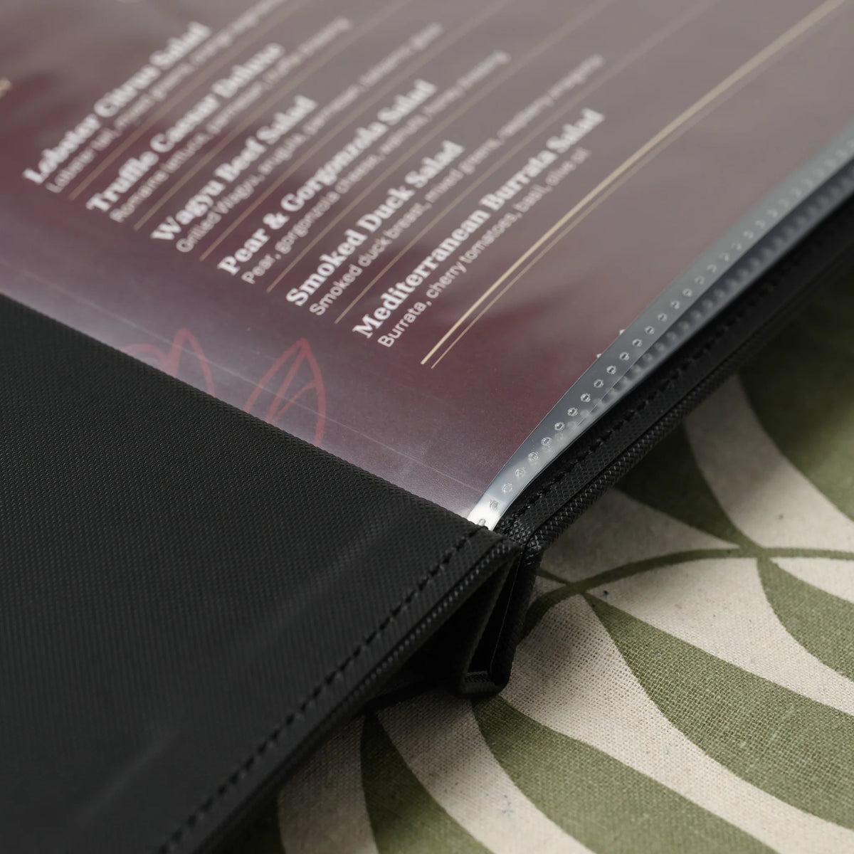 Close-up of the heat-sealed edges of clear plastic sleeves at the spine of a black textured faux leather menu cover