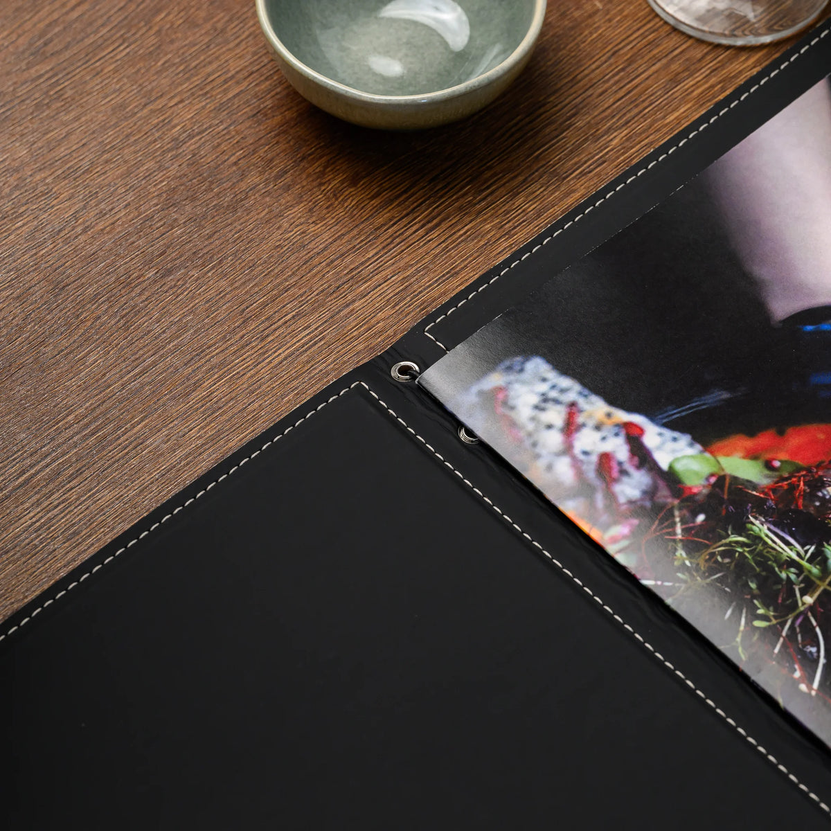 Open folder interior with black lining, light stitching and two silver eyelets beside a food photo menu page