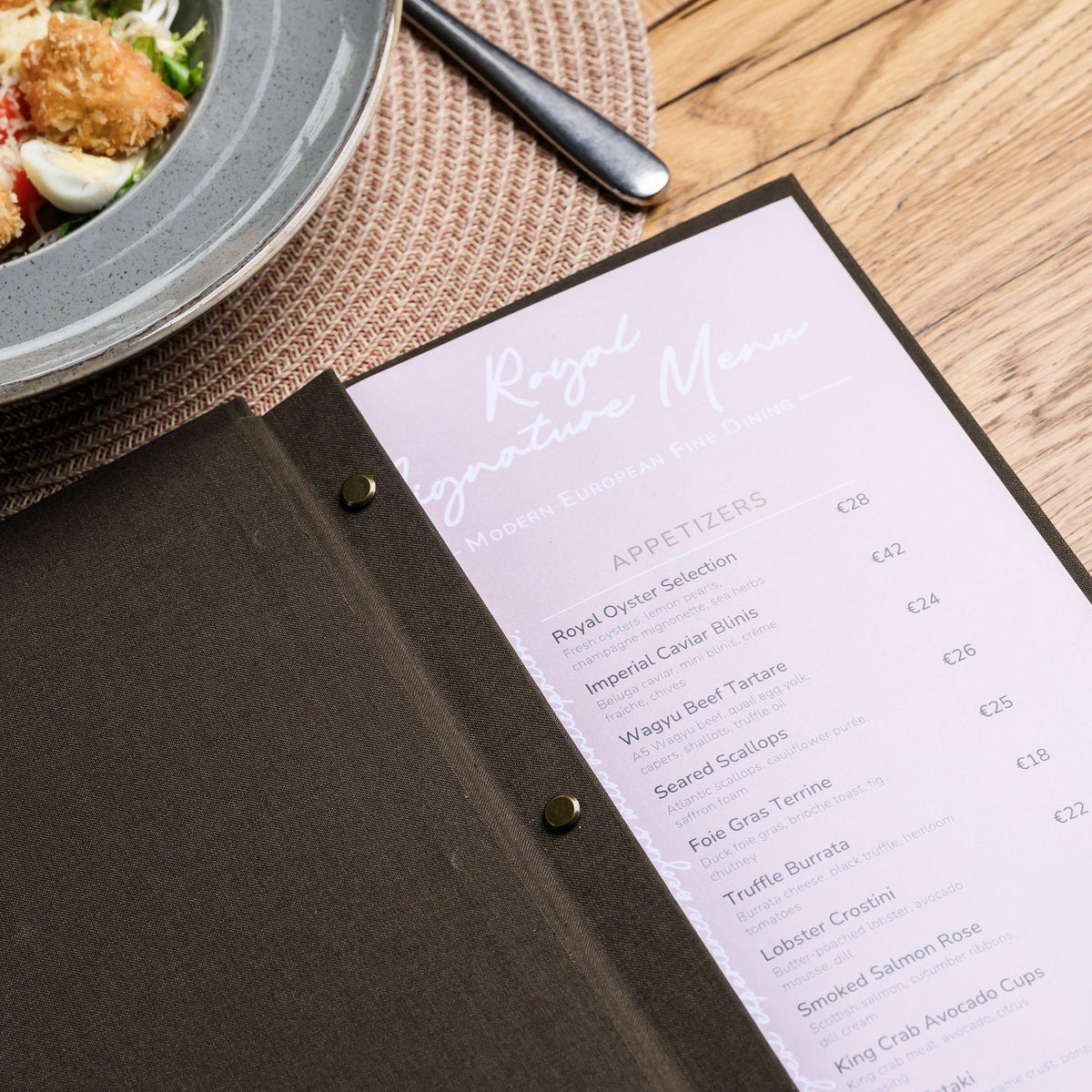 Wide open espresso-brown textile menu folder with a lavender printed menu page beside a blurred salad plate