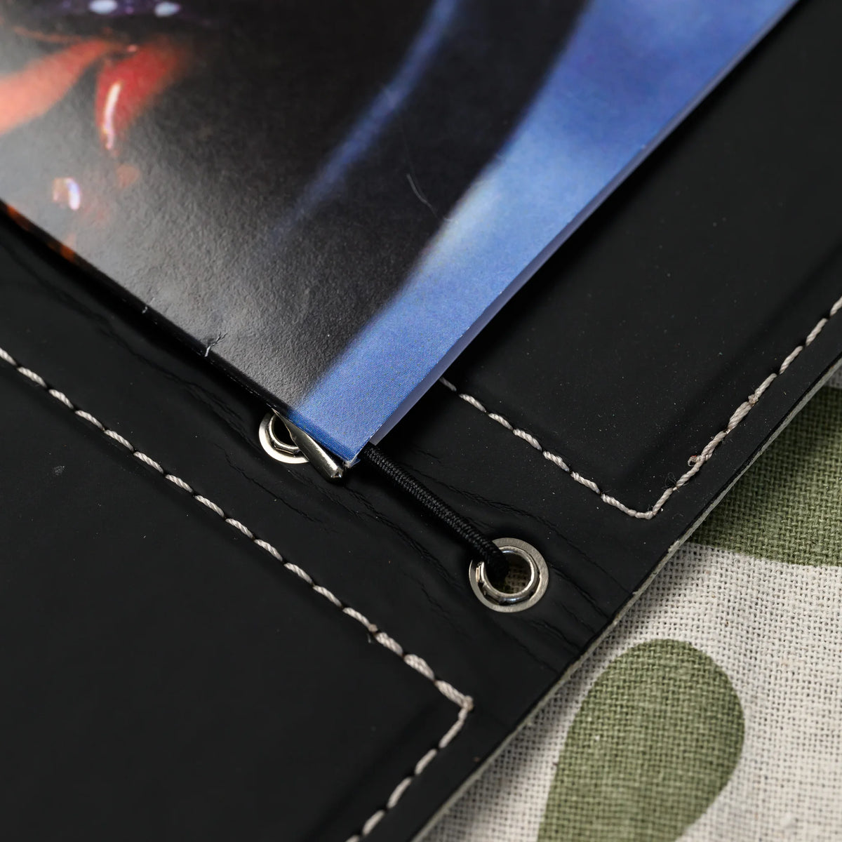 Macro of elastic cord passing through silver eyelet with a metal stopper at the spine holding folded pages