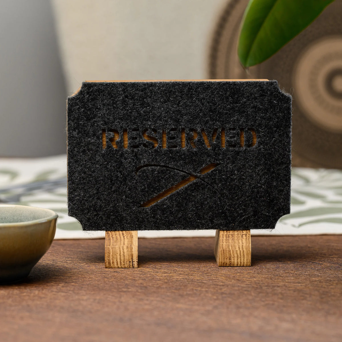 A close-up of a Reserved table sign with die-cut felt lettering standing near a small ceramic teacup