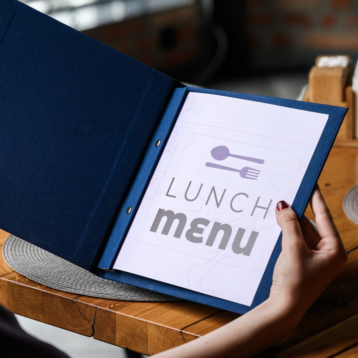 Hand holds a wide open navy textile menu folder with a white lunch menu title page on a wooden table