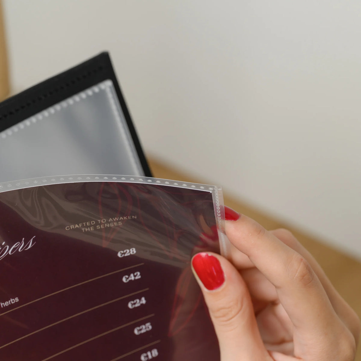 Hand sliding a clear plastic sleeve with a printed menu page out of a black menu cover with an empty sleeve behind