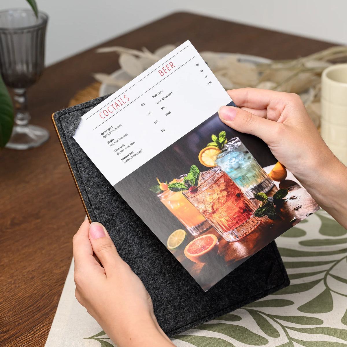 Hands holding a felt menu clipboard that displays a printed page secured by its corner slots closely