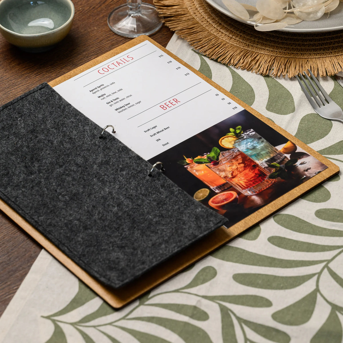 A ring-bound menu board lying fully open on a fully set restaurant table, displaying a printed menu page