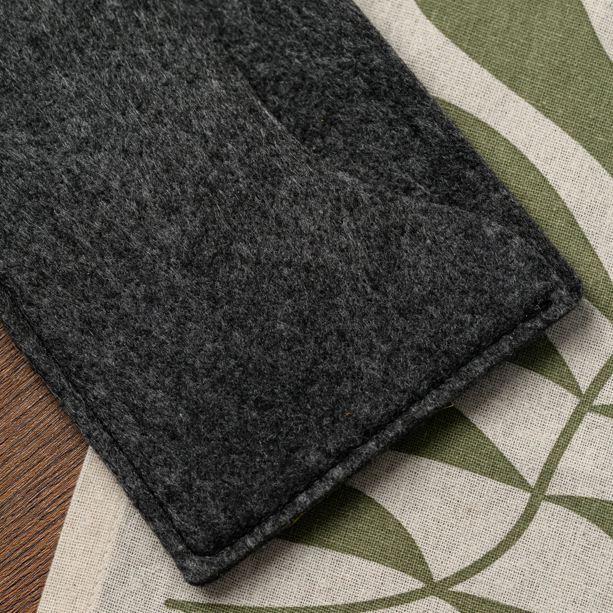 A macro view of the stitched felt corner of a bill presenter resting on a patterned linen tablecloth