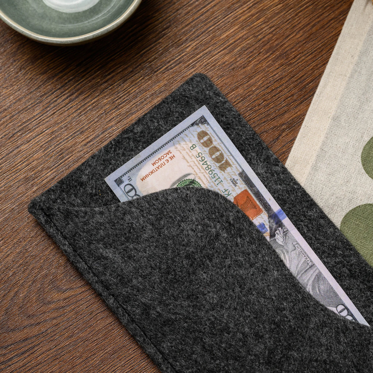 An overhead view of a banknote tucked into the wavy felt pocket of a bill presenter on the wood table