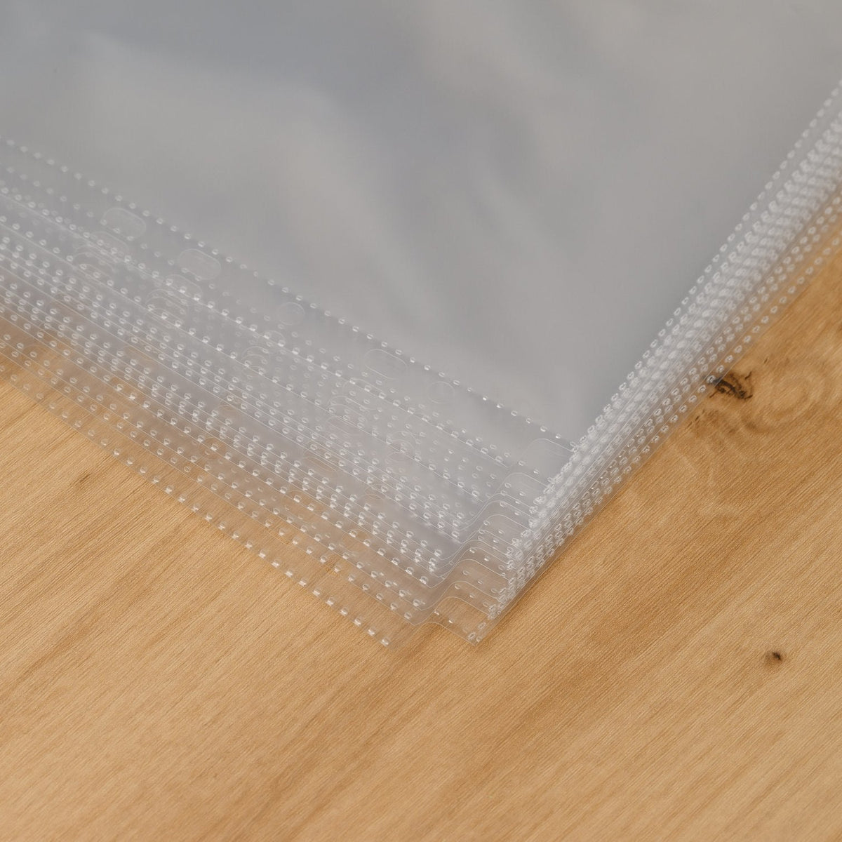 Corner of a stack of clear menu sleeves showing heat-sealed dotted seams along the edges of each sheet protector