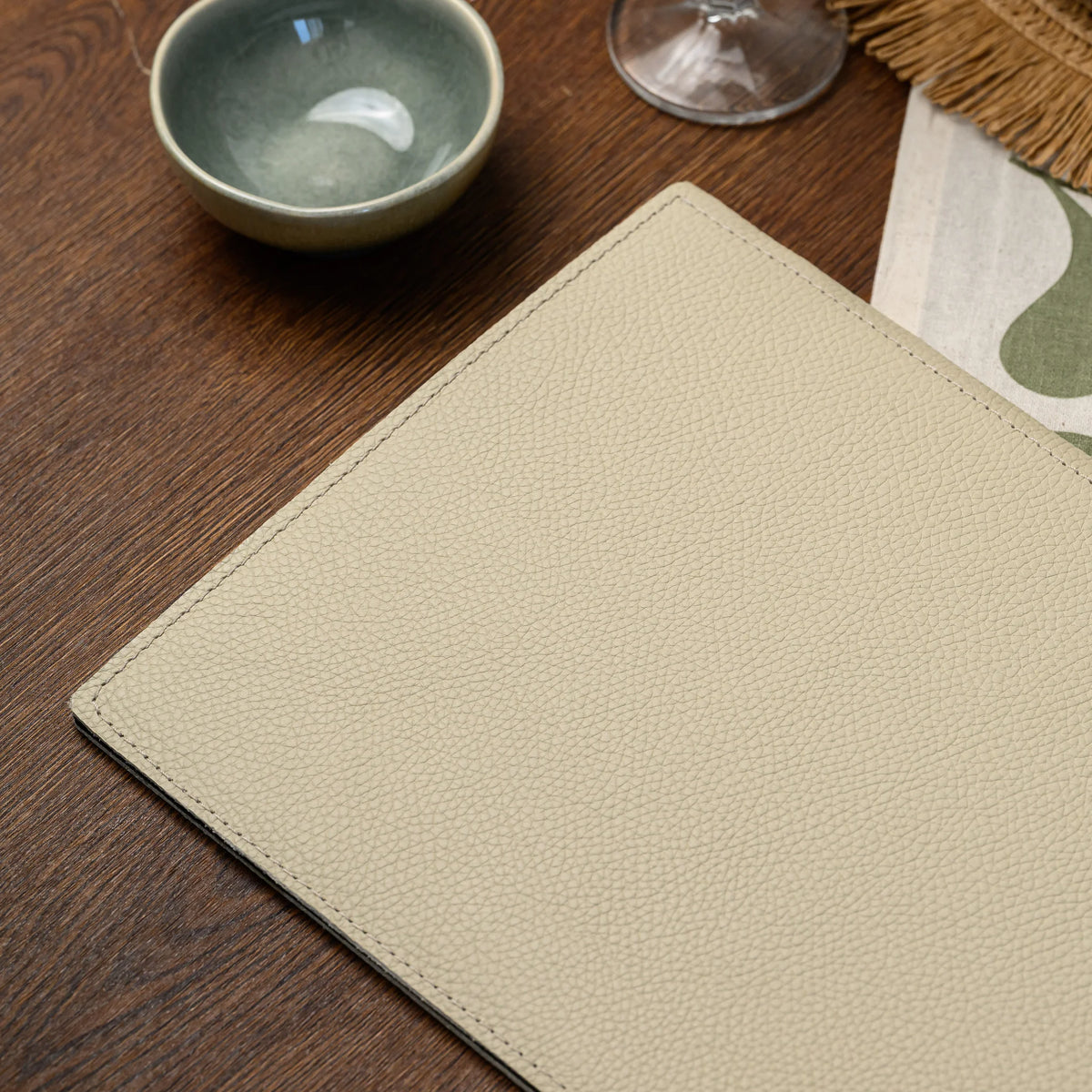 Plain beige leather menu cover without a logo plate on a wooden table next to a ceramic bowl, stitched border