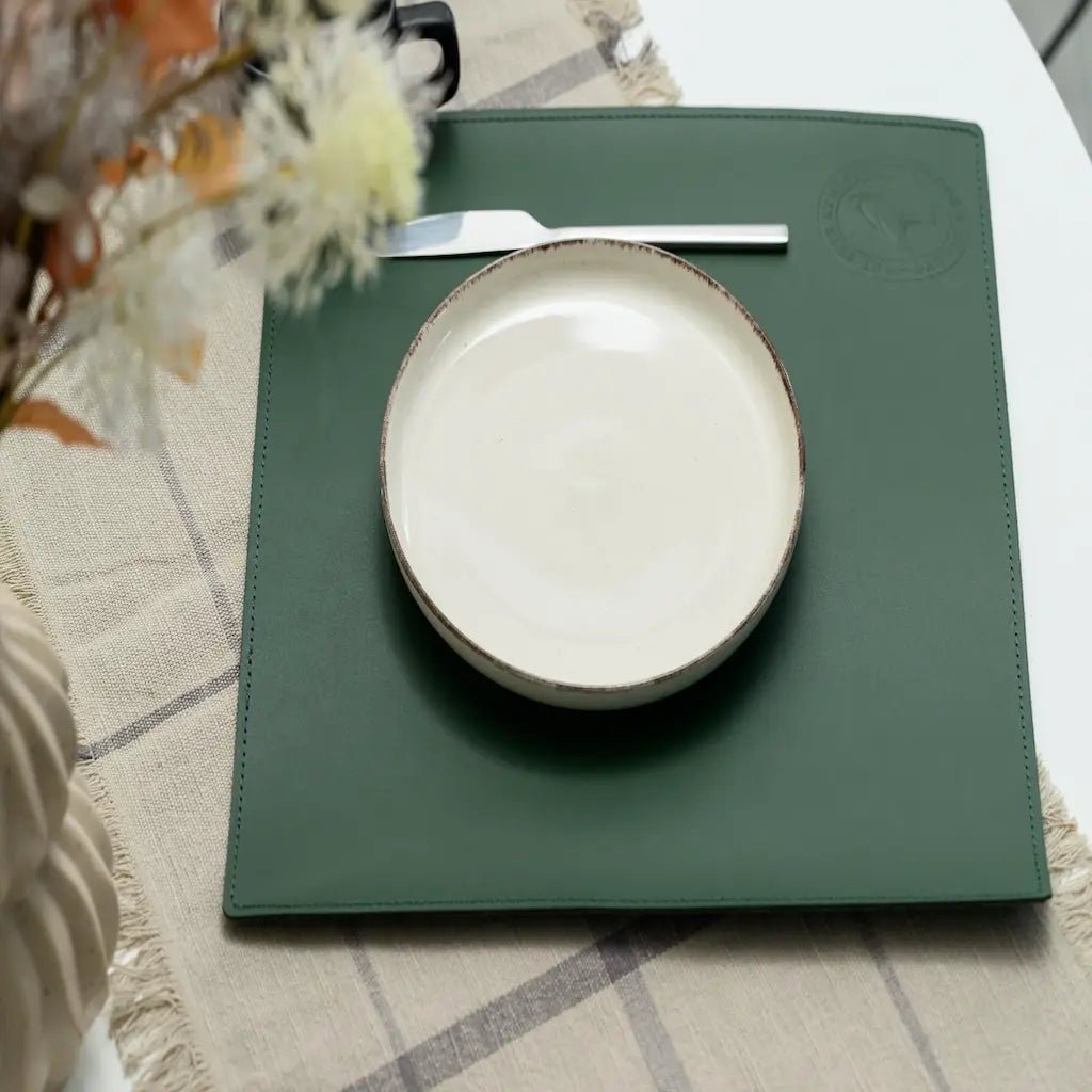White ceramic plate on a green placemat with a knife and fork, on a textured tablecloth.