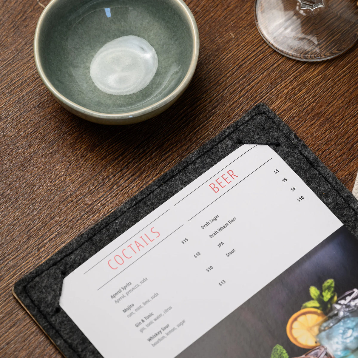 A felt menu clipboard lying open on a restaurant table, holding a printed page beside a ceramic bowl