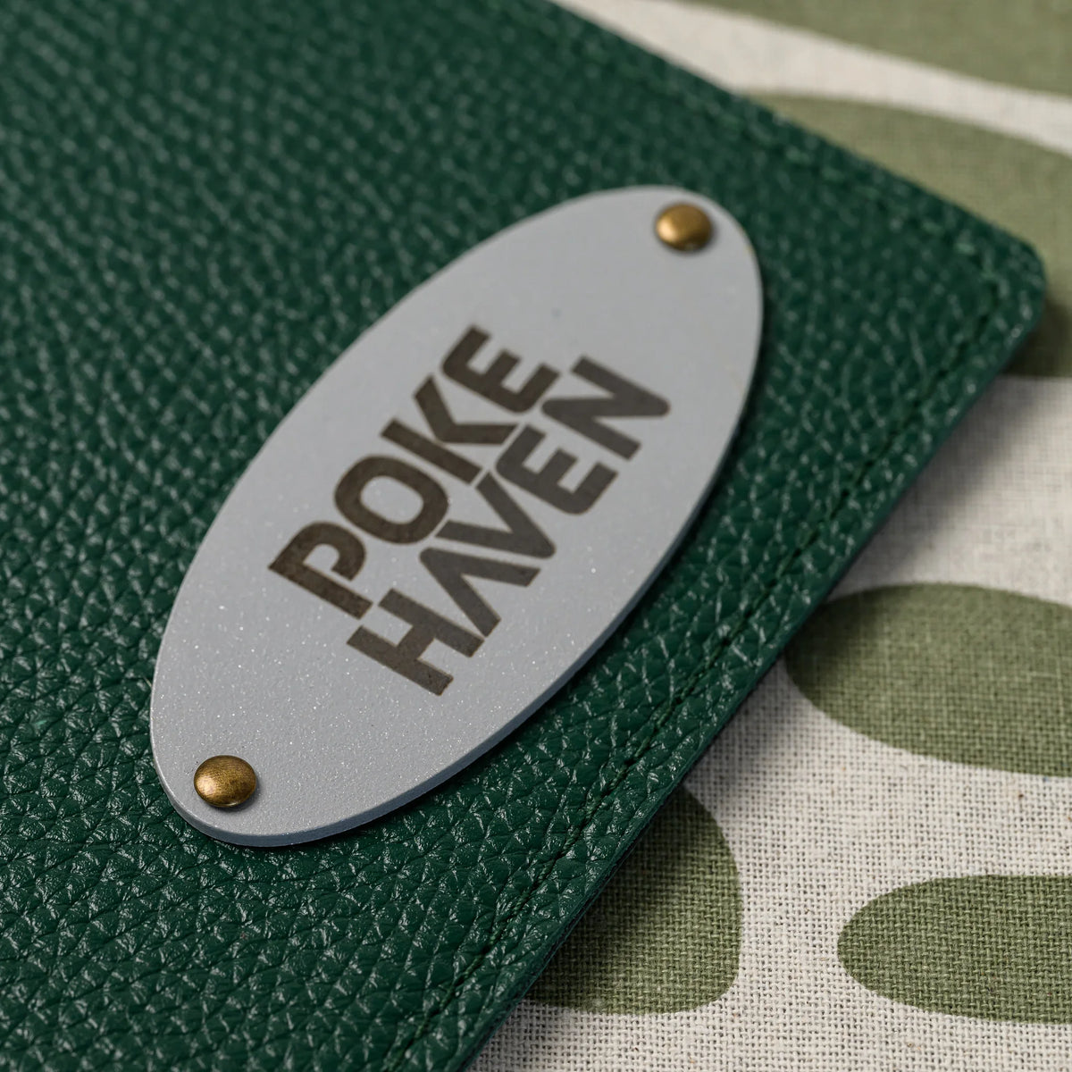 Macro of an oval silver metal plate with engraved logo attached to pebbled green leather with brass rivets