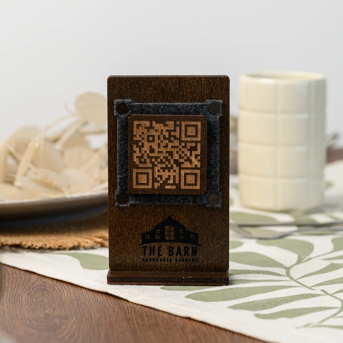 A freestanding wooden QR code table stand with a felt-framed panel, displayed beside a small ceramic mug