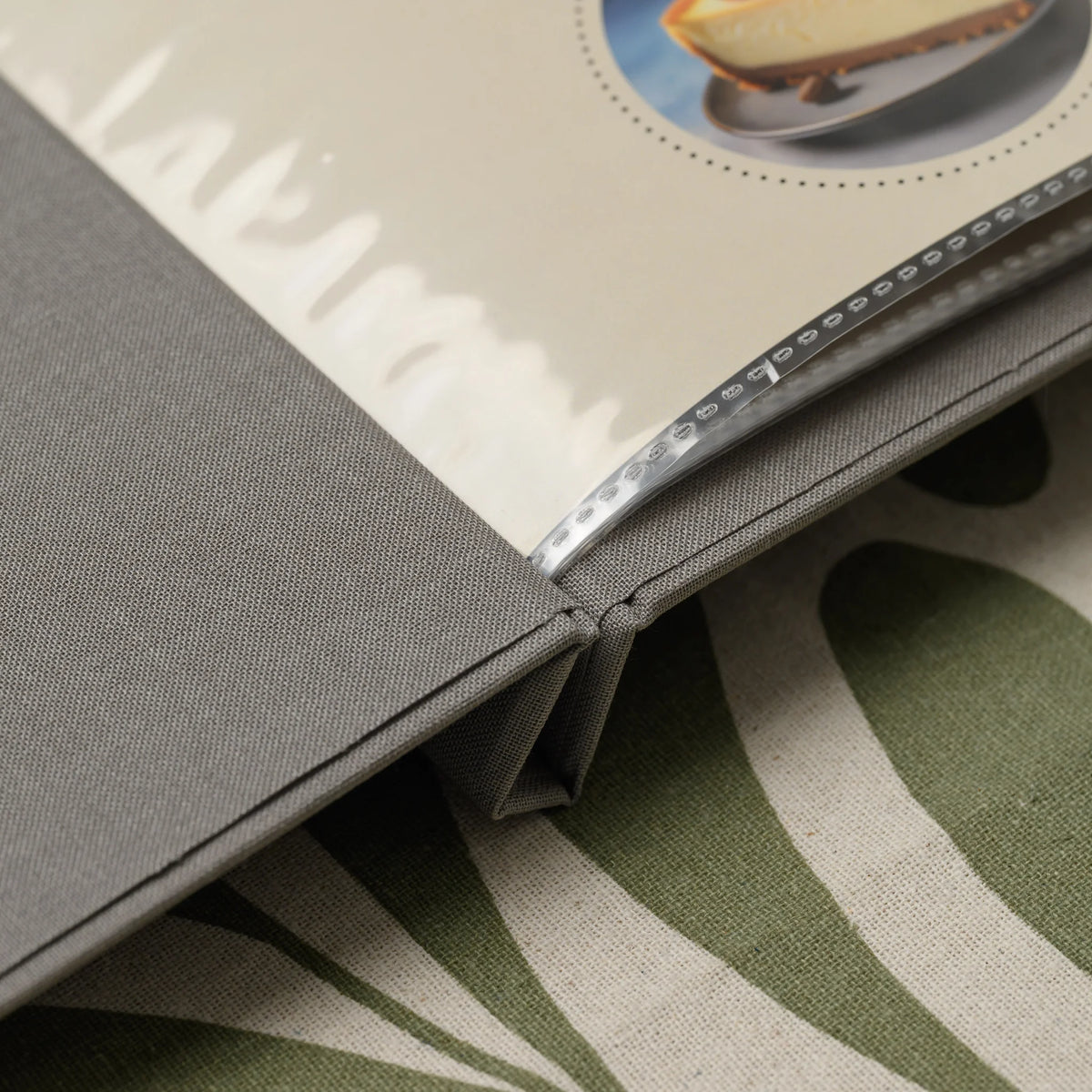 Close-up of the spine of a gray fabric menu cover with clear plastic sleeves and their heat-sealed dotted edges