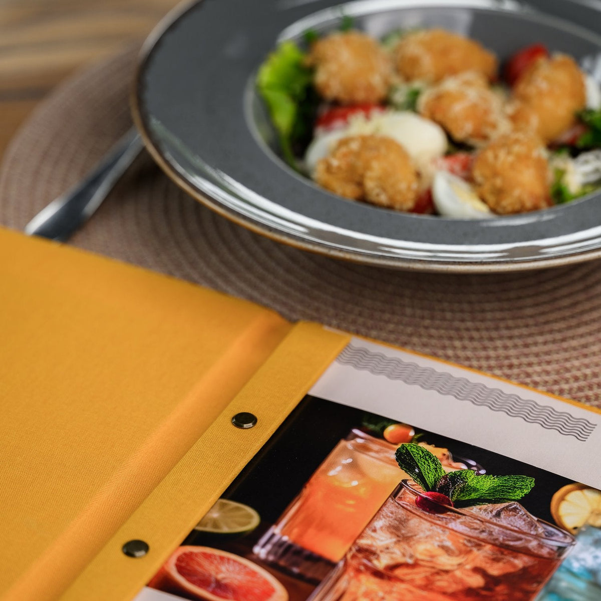 Open mustard-yellow textile menu folder shown from the side with a bar binding rail and a food photo insert
