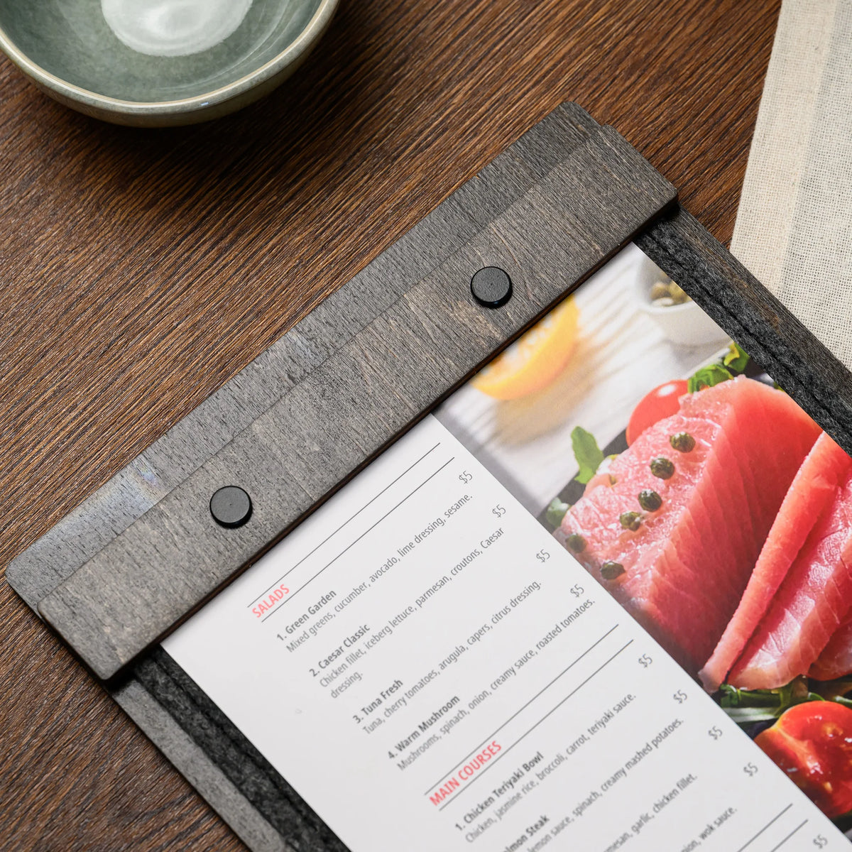 A close-up of a screw and clamp bar holding a printed menu page against the felt board surface closely