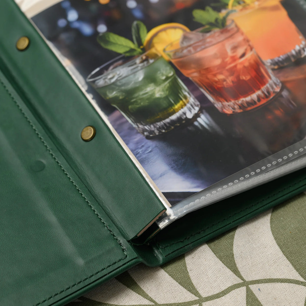 Close-up of the screw post plank inside a green menu cover with brass screws and the sealed edge of a plastic sleeve
