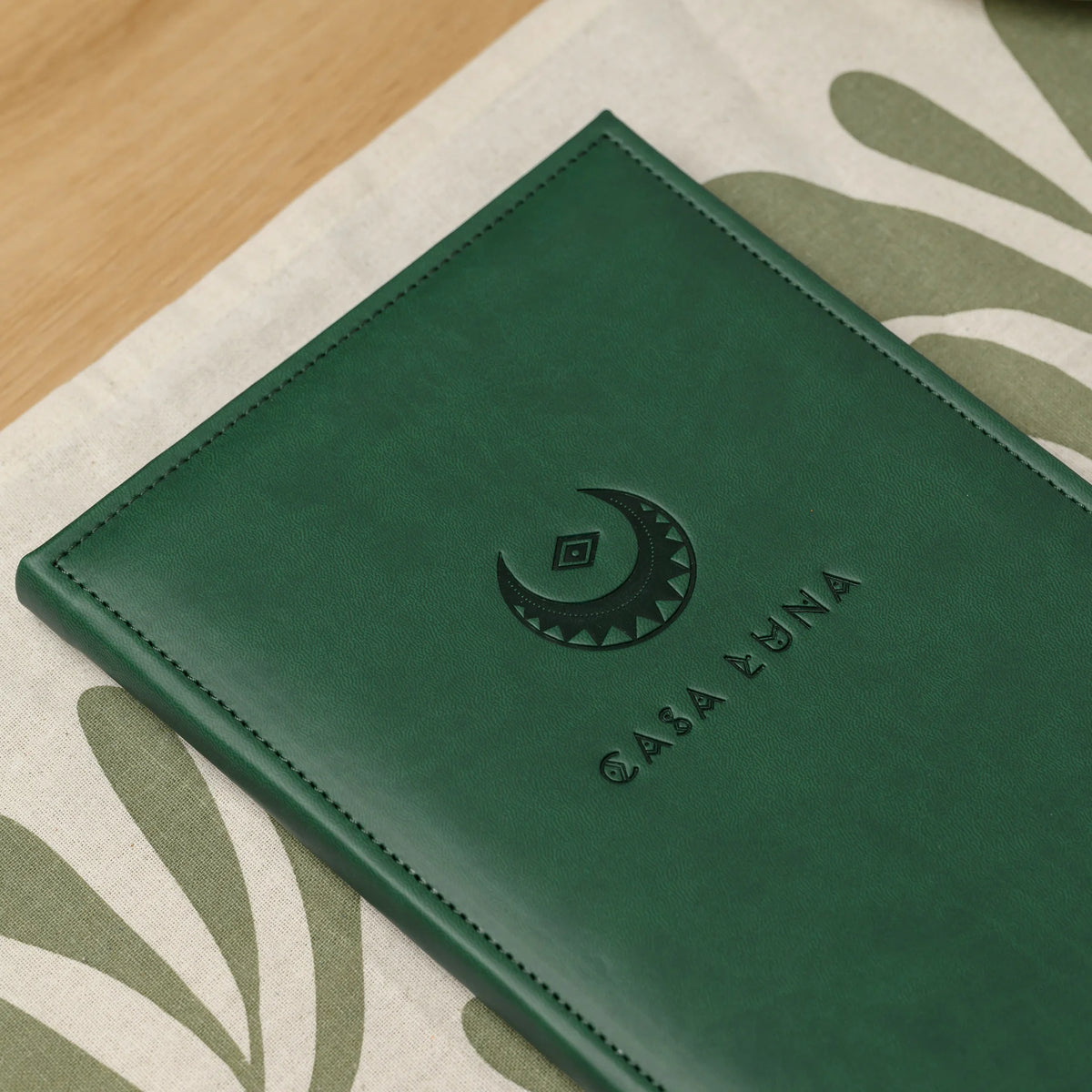 Close-up of a blind embossed crescent logo and lettering on the front of a green Soft Touch faux leather menu cover