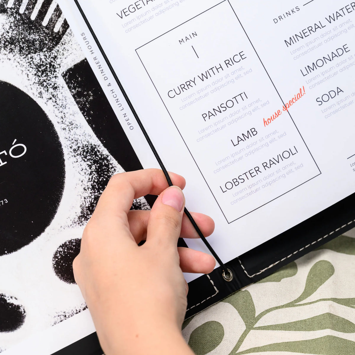 Hand lifting the black elastic cord to slide printed menu pages into an open folder with black inner lining