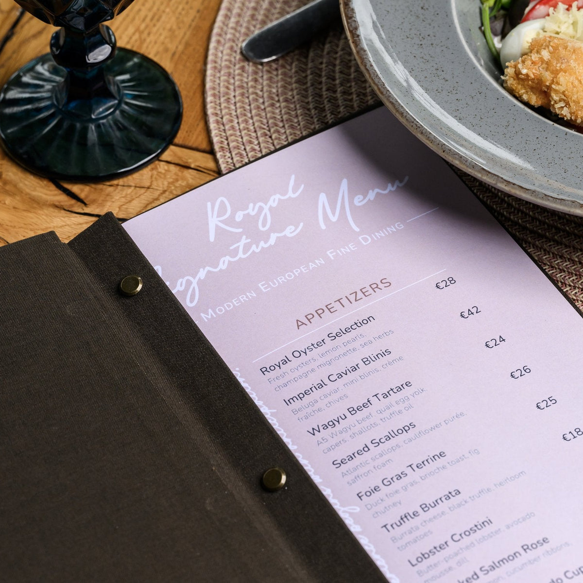 Closed espresso-brown textile menu folder standing upright with a cursive logo on a grey woven placemat
