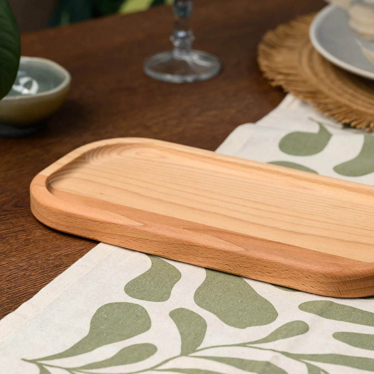 Angled view of an empty beech wood rectangular serving board on a dark table beside a wine glass and plate