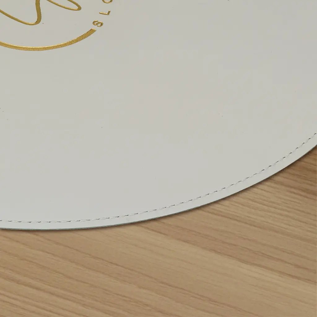 Round white placemat with gold border on a wooden surface