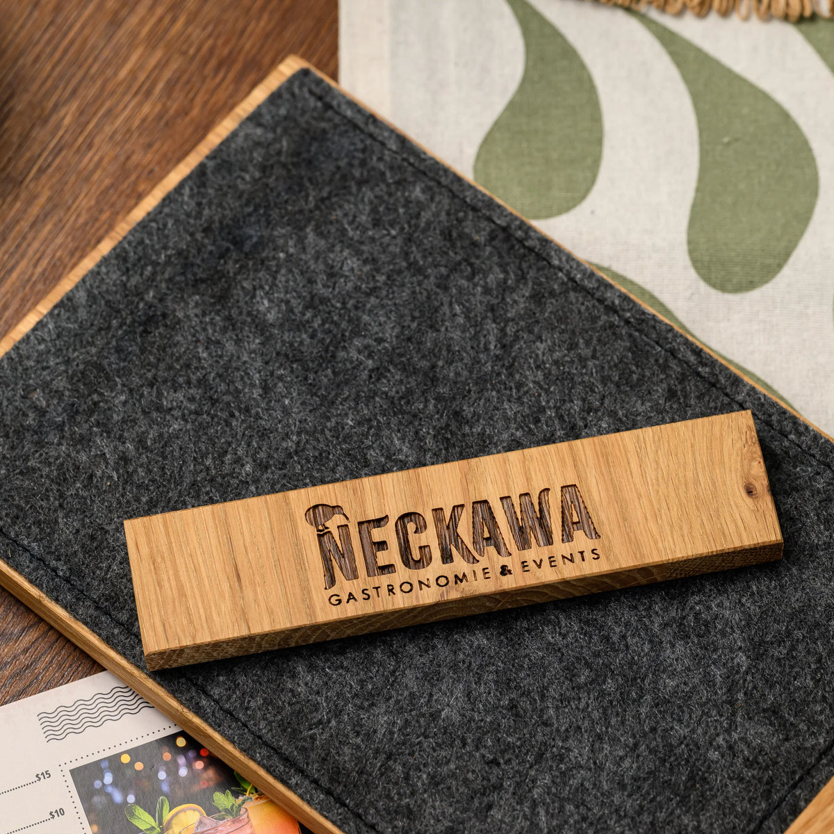 A close-up of an engraved oak bar resting against a felt panel, with the logo cut directly into the wood