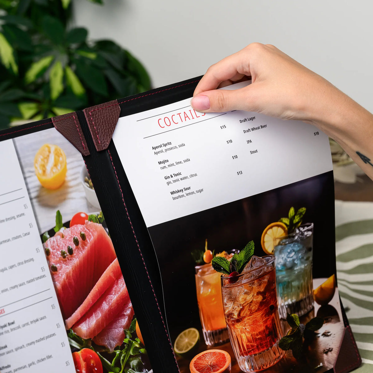 Hand sliding a printed cocktail menu sheet out of the bordeaux leather corner mountings of an open cover