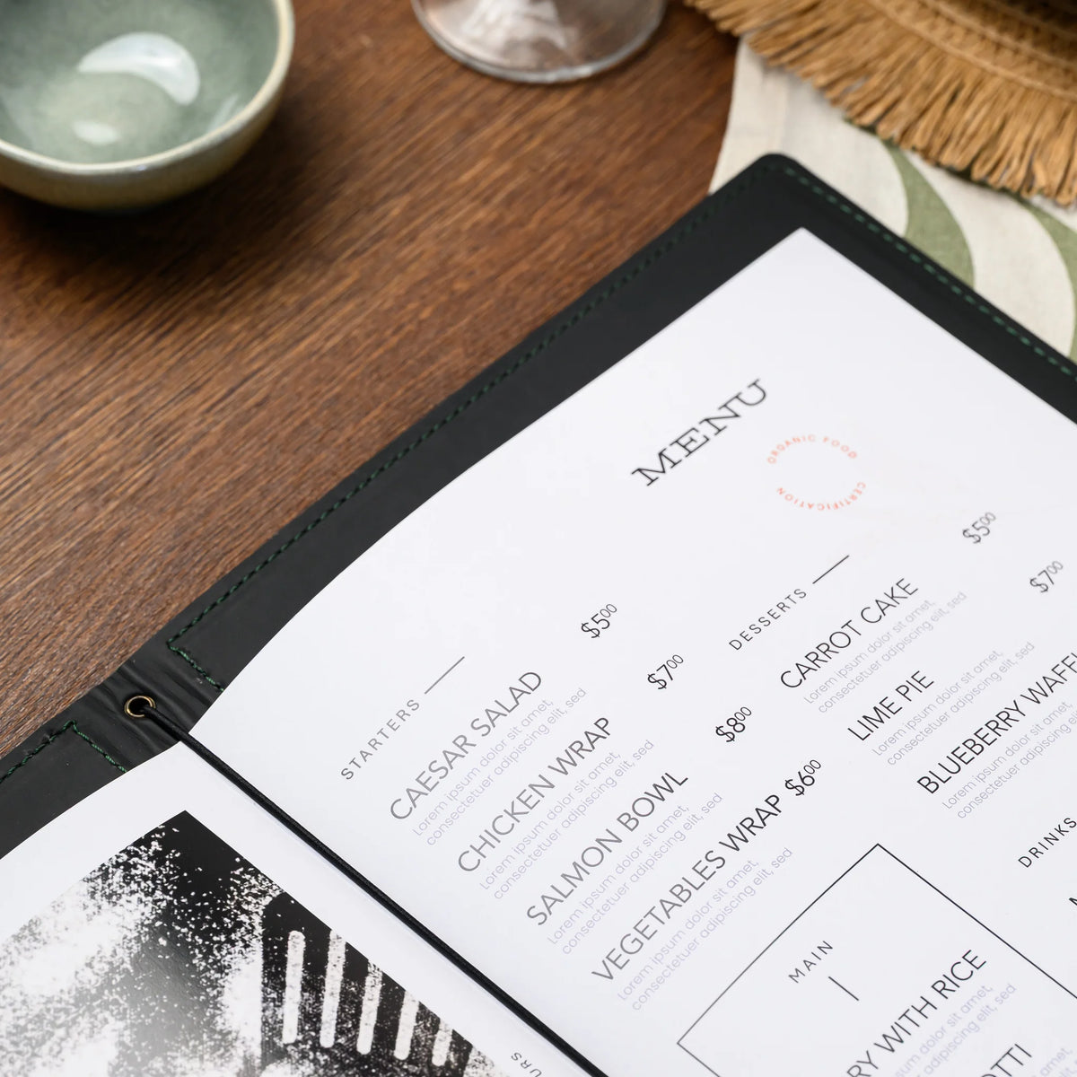 Open menu folder on a wooden table with printed menu pages held by black elastic cord running through eyelet
