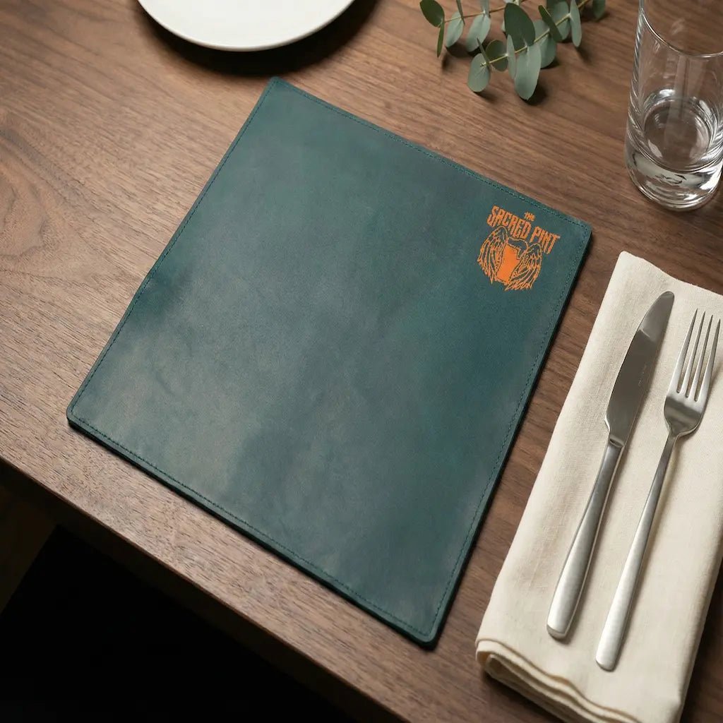 Green placemat with a logo on a wooden table with cutlery and a glass.