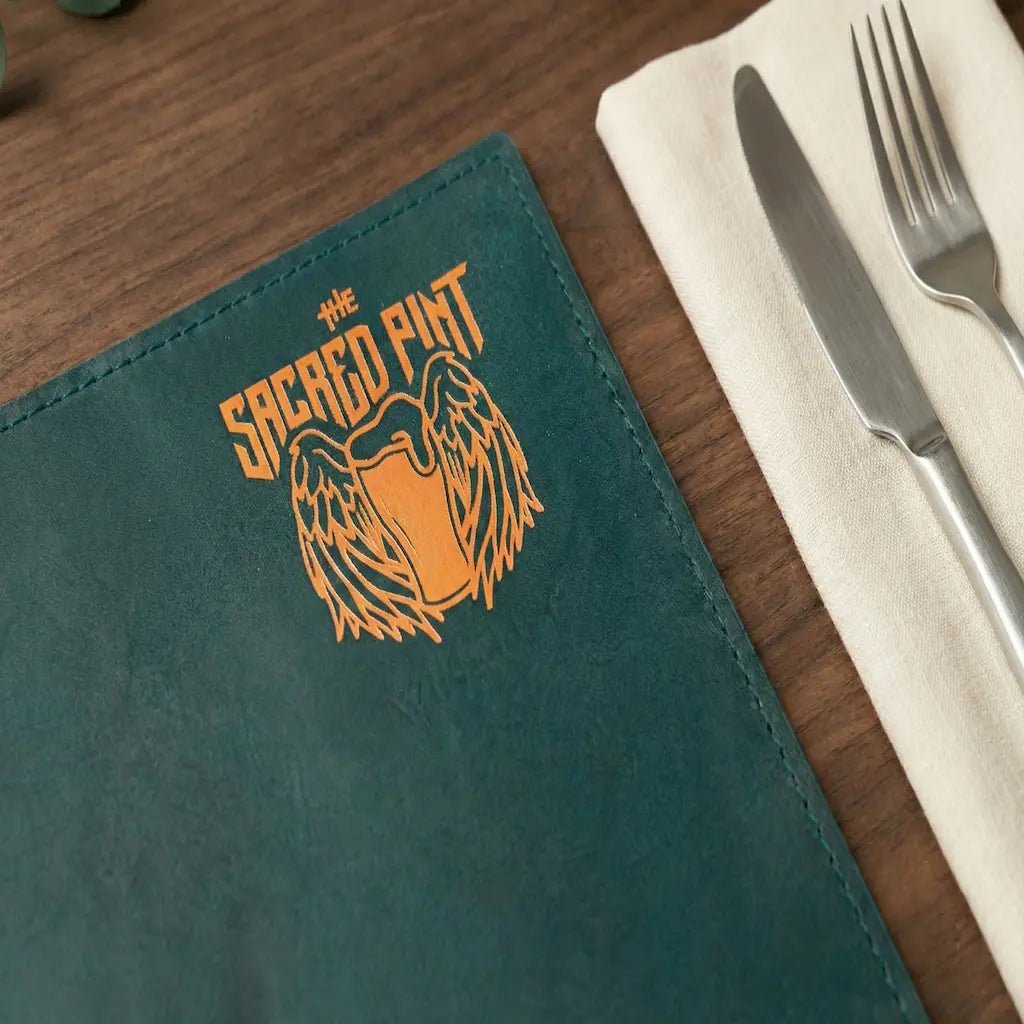 Green menu with 'The Sacred Pint' logo on a wooden table with cutlery.