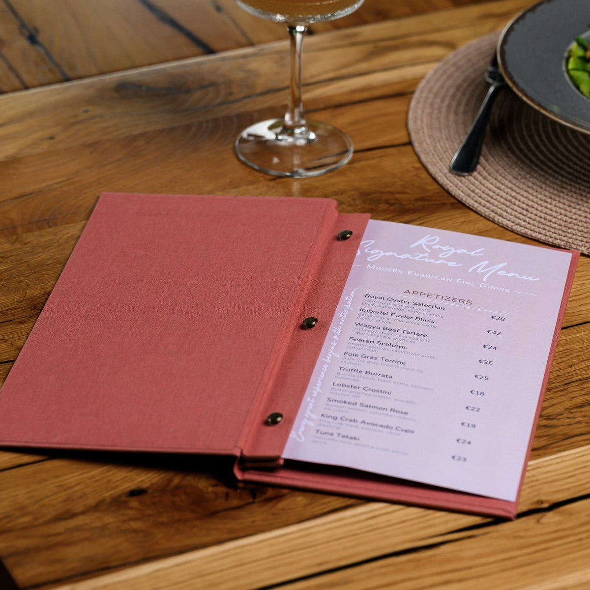 Wide open coral-pink textile menu folder with a lavender printed menu page on a wooden restaurant table