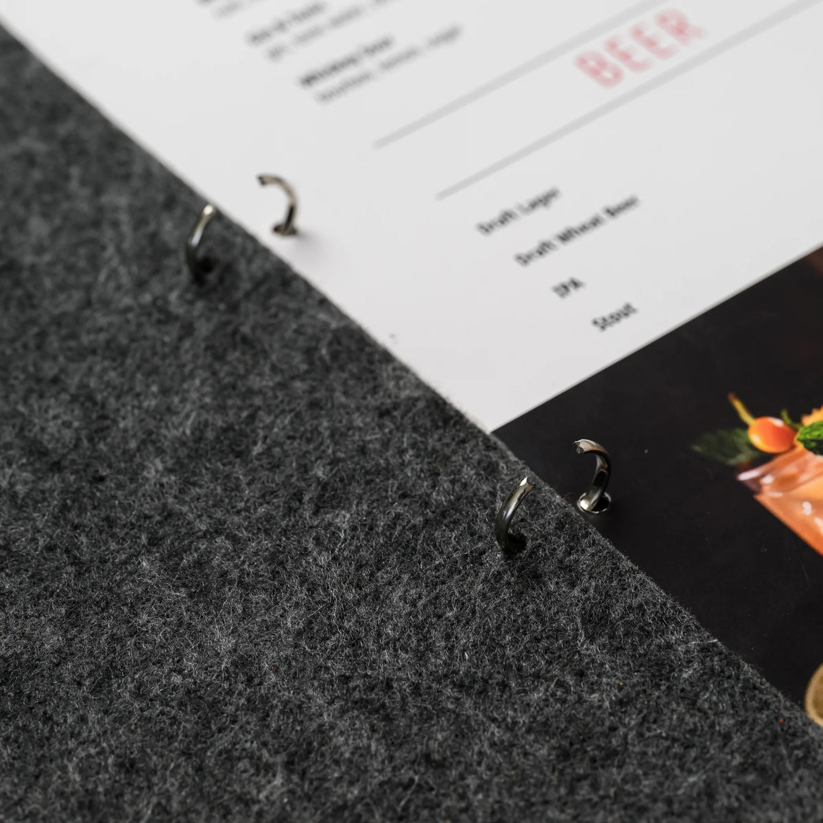 A macro view of a metal ring mechanism holding a printed menu page in place against the felt cover panel