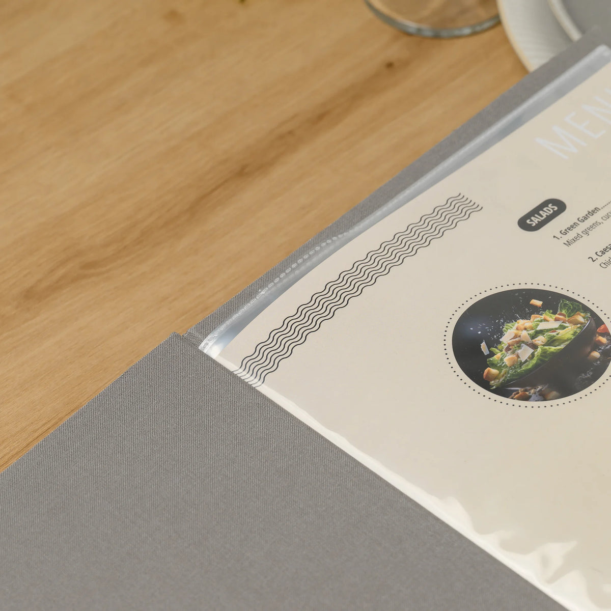 Close-up of the spine of a gray fabric menu cover with clear plastic sleeves and their heat-sealed dotted edges