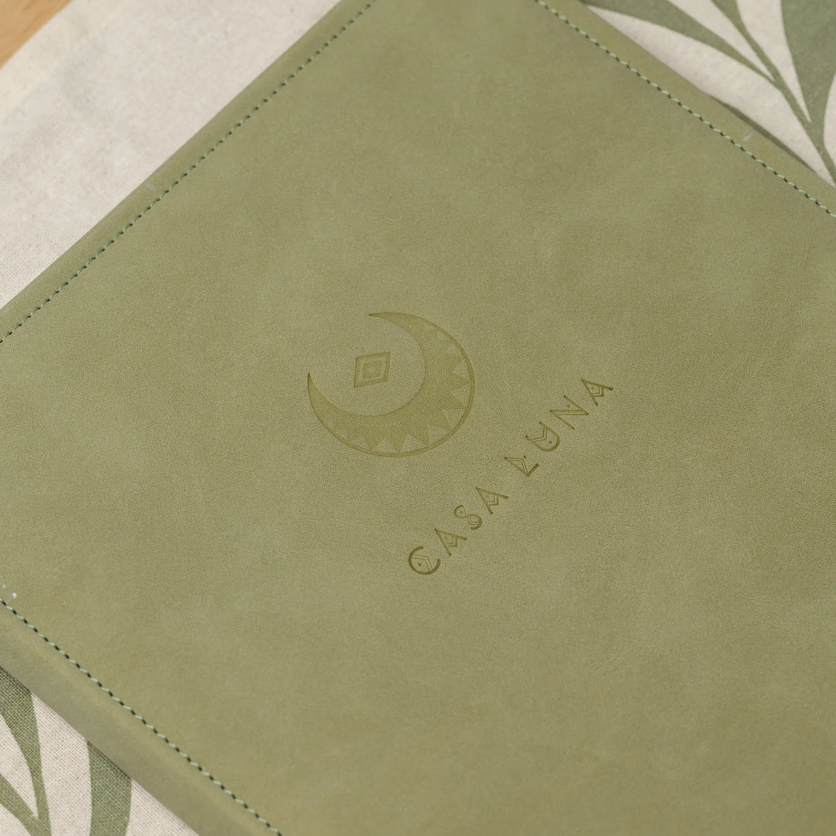 Close-up of a blind embossed crescent logo and lettering on the velvet-like surface of an olive Nubuk menu cover