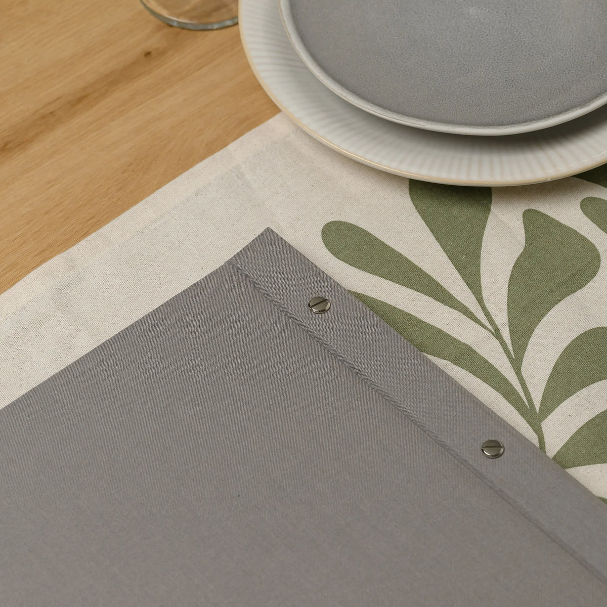 Corner of a gray fabric menu cover with two chrome screw heads on the spine lying on a patterned table runner