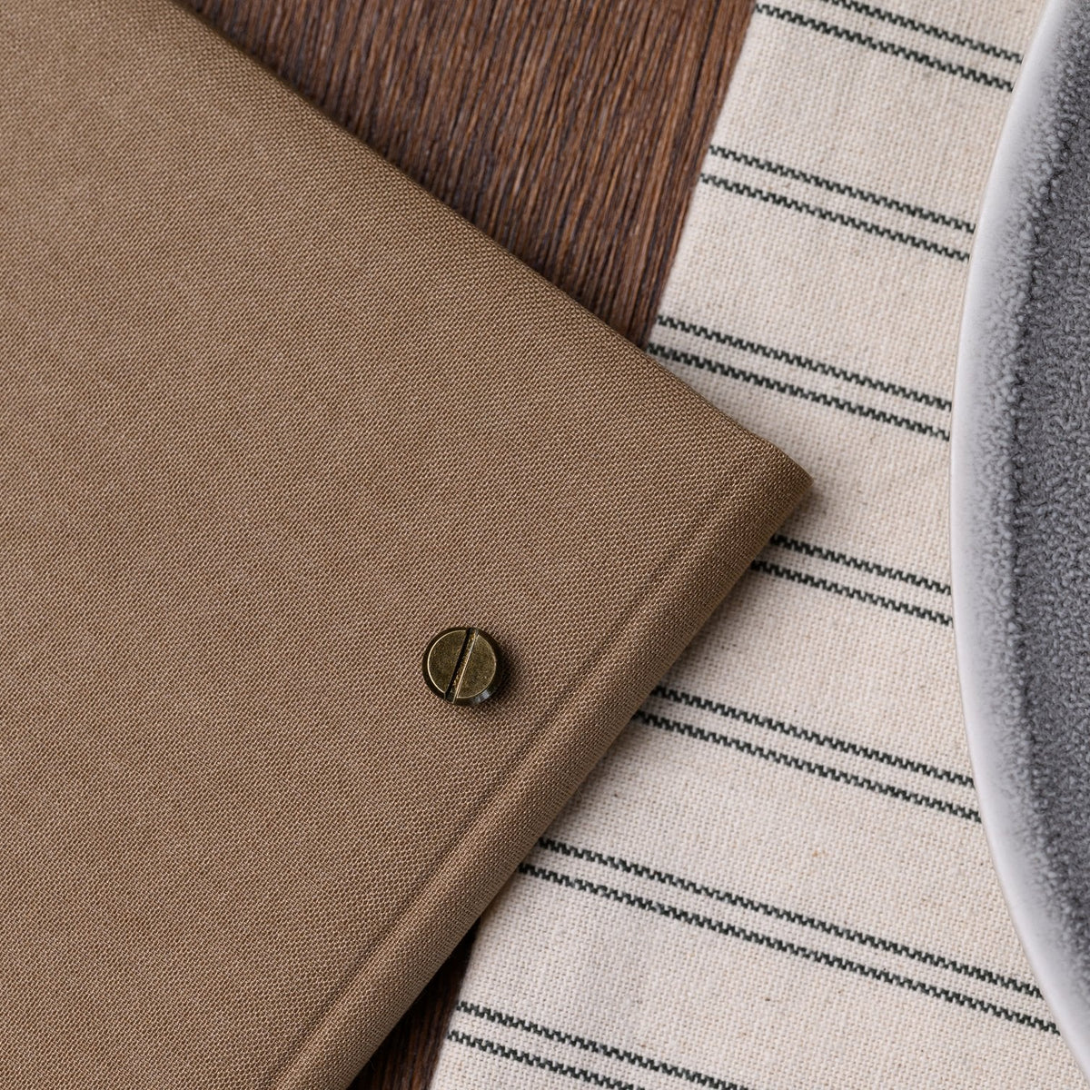 Closed taupe textile menu folder standing upright with a bar binding rail visible on a striped placemat