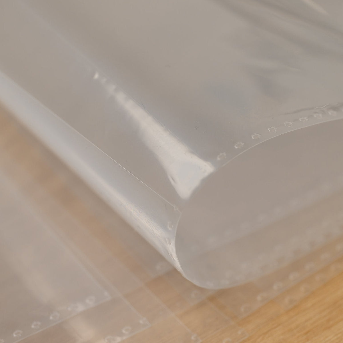Open top edge of a clear plastic menu sleeve curled up to show the pocket where a printed menu page slides in