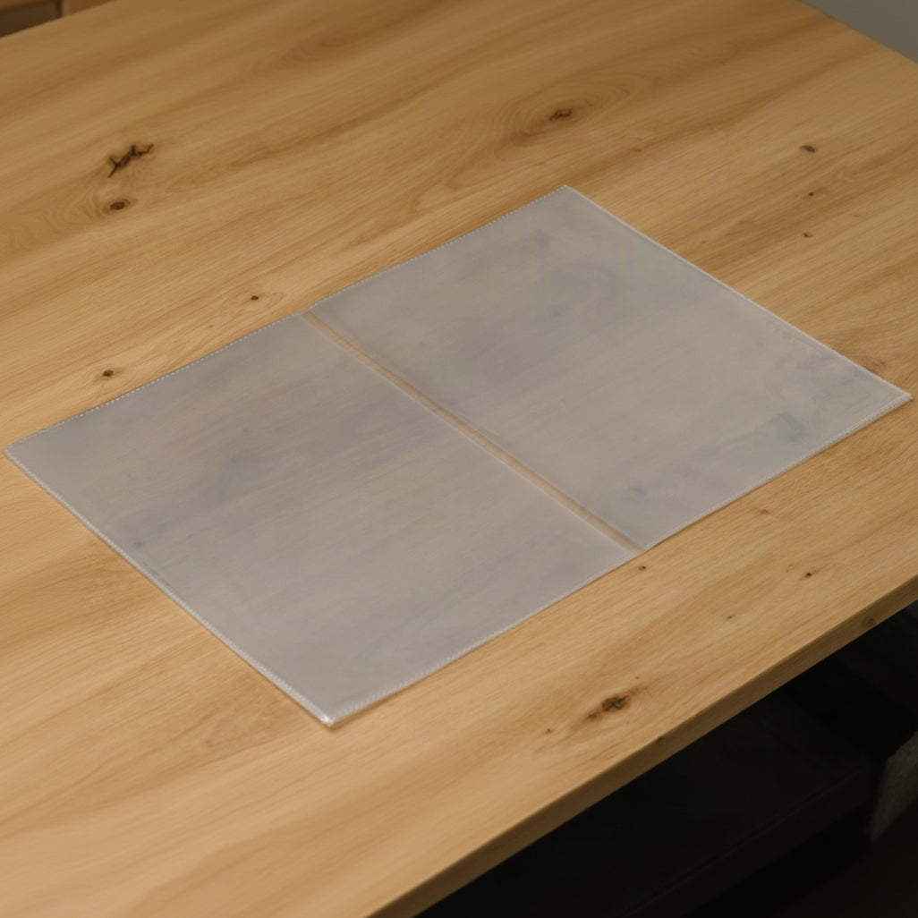 Center-fold plastic menu sleeve opened flat on a wooden table, two clear panels joined by a fold in the middle