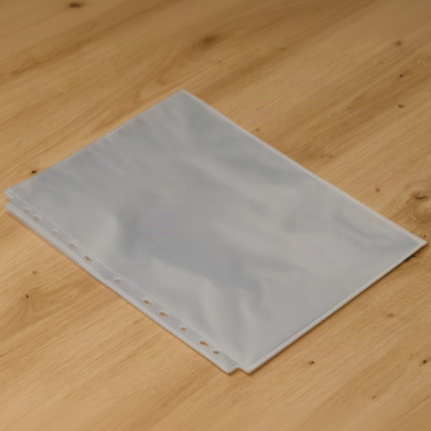 Stack of clear plastic menu sleeves with punched holes along the long edge lying on a light oak wooden table