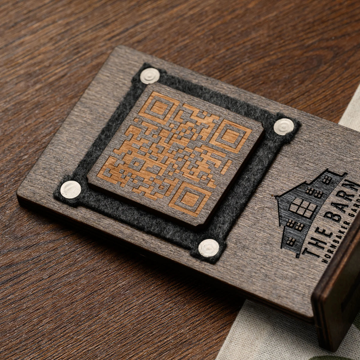 Side profile view of a wooden QR code table stand showing the felt frame edge and engraved logo detail