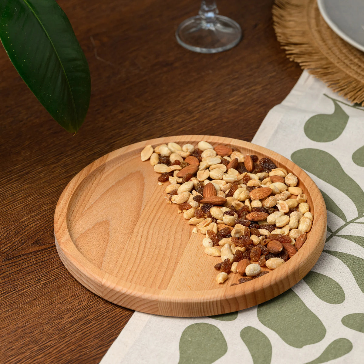 Overhead view of the round beech wood serving plate styled with scattered nuts, raisins, and almonds