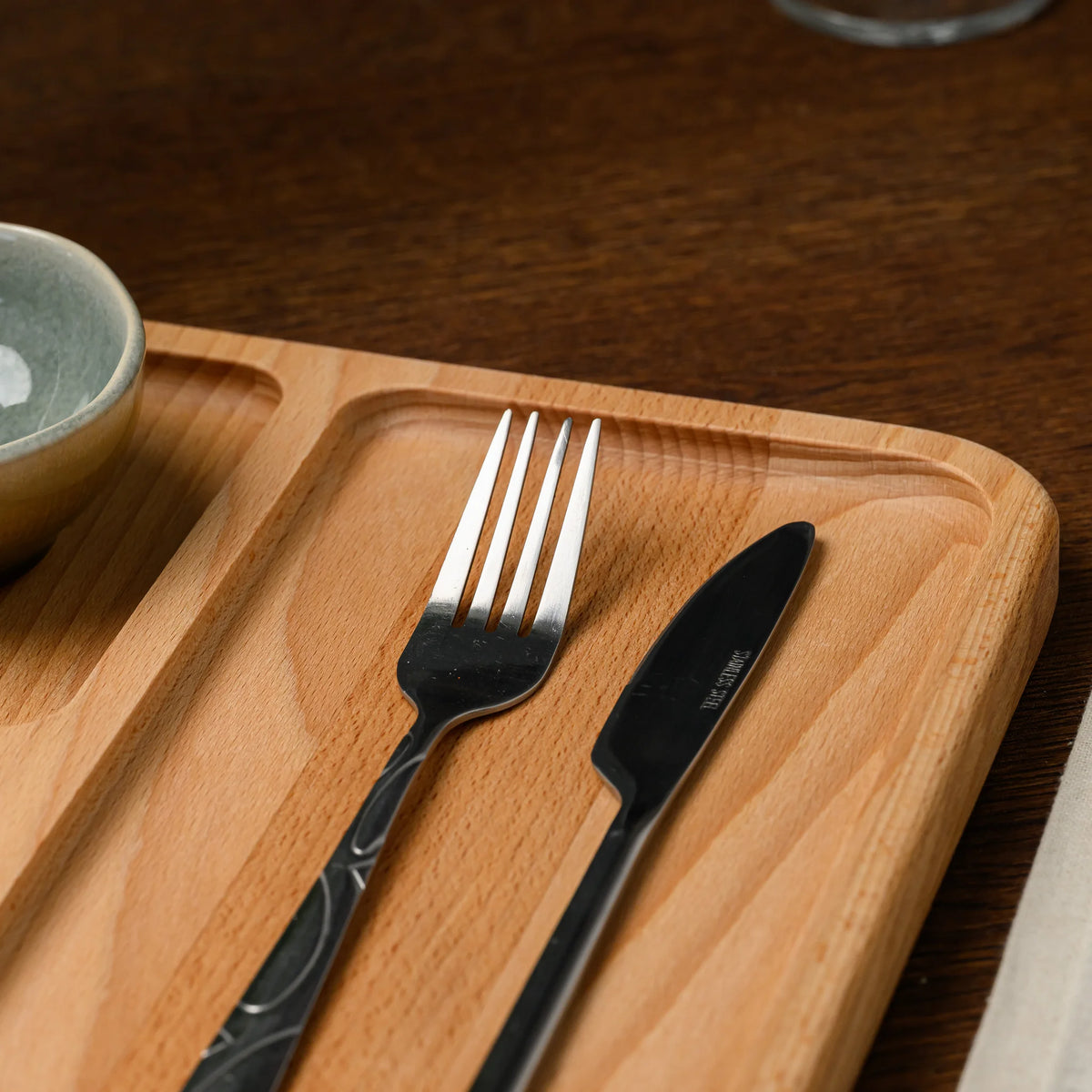 Fork and knife resting in the cutlery compartment of the beech wood board, with a ceramic bowl in the corner
