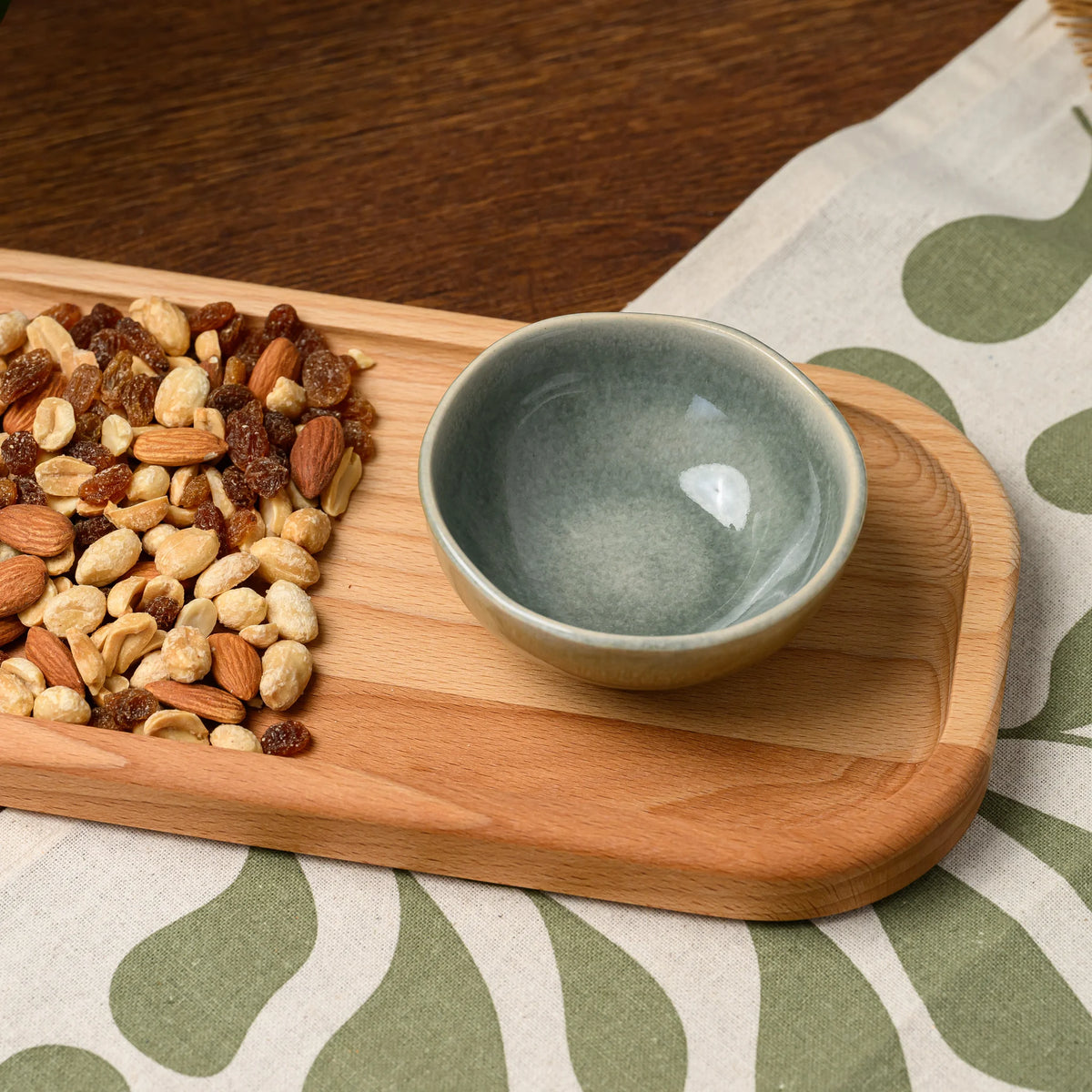 Overhead view of mixed nuts and raisins beside an empty ceramic bowl on the beech wood rectangular board