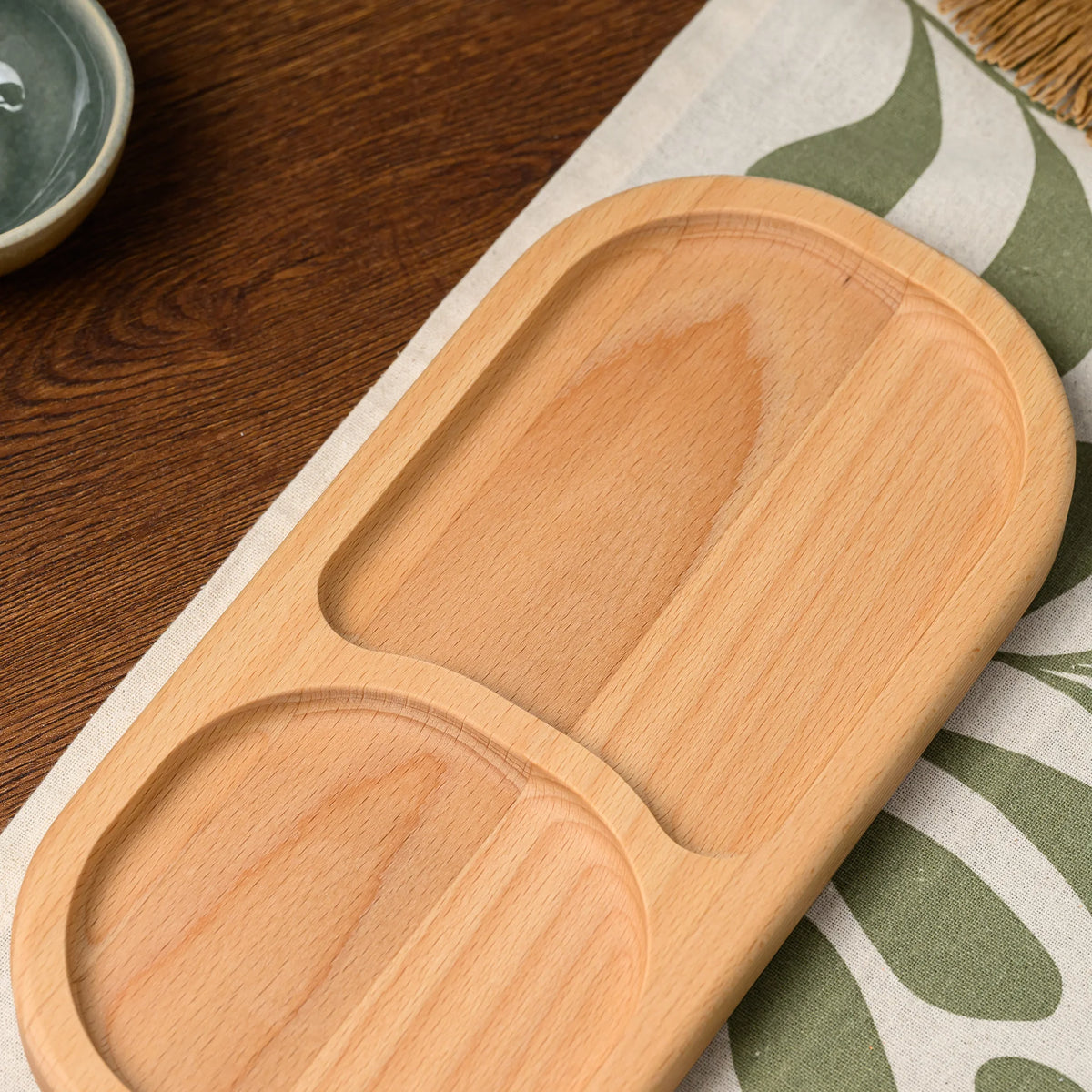 Close-up overhead view of two empty oval compartments on the beech wood divided serving board, grain visible